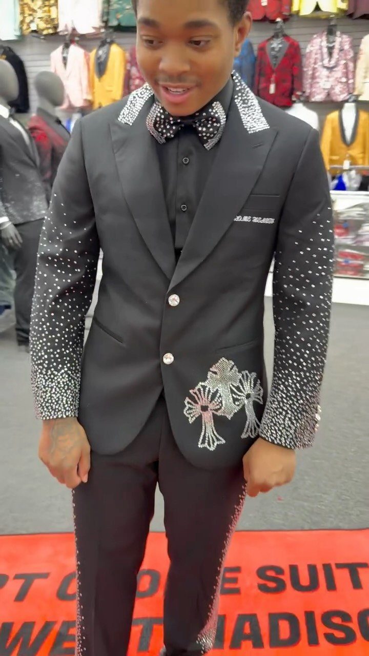 Young man posing in a black tuxedo decorated with sparkling silver embellishments and a bow tie.