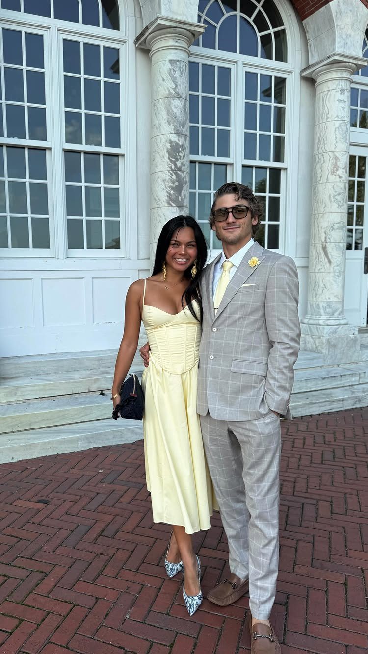 A woman in a yellow midi dress and a man in a grey suit posing together.