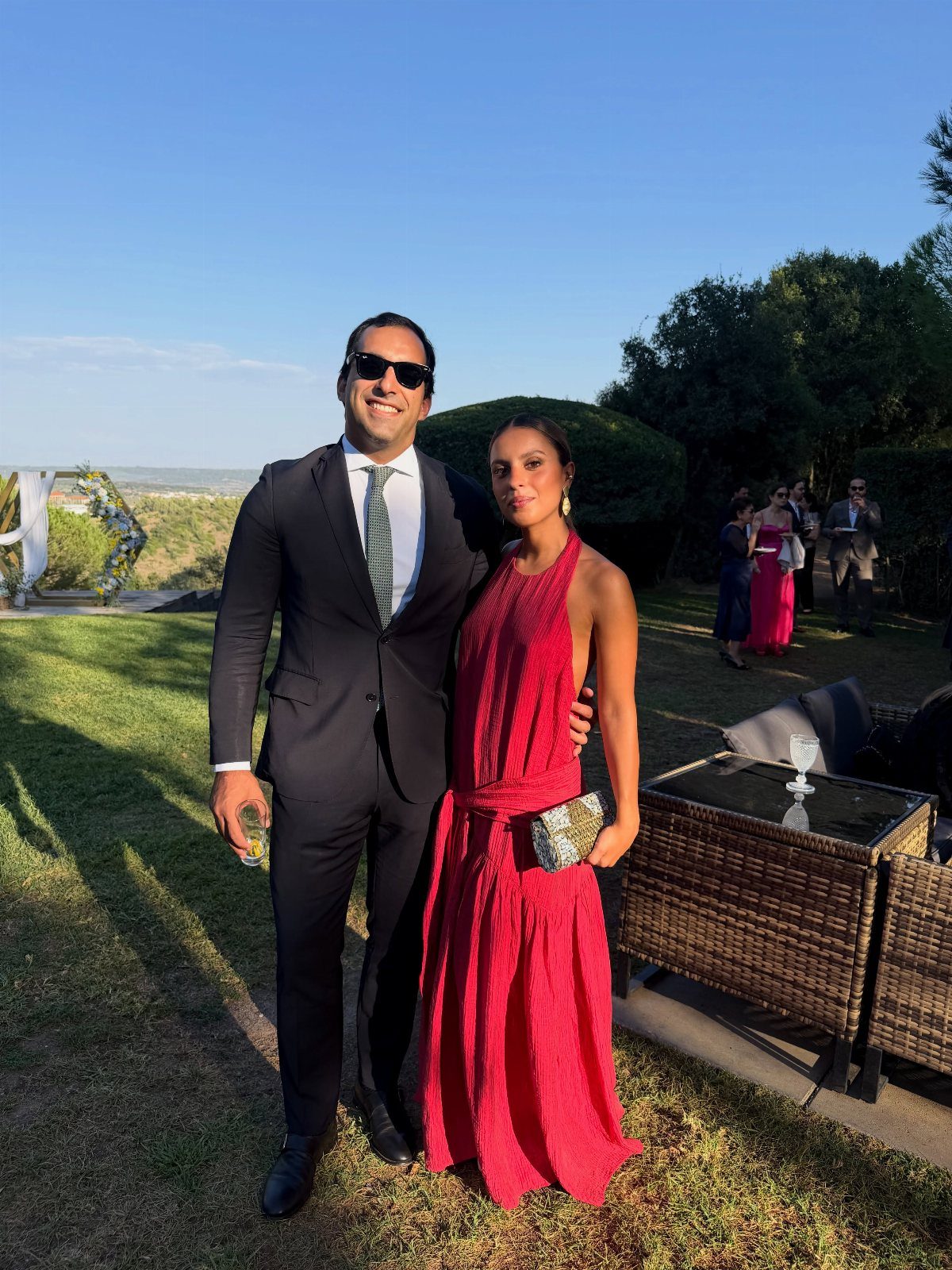 A man in a dark suit and a woman in a long red dress posing outdoors.