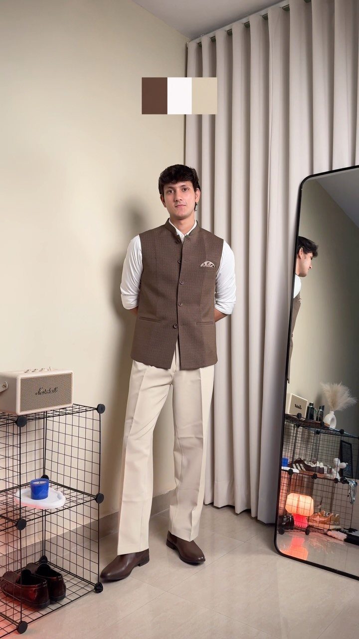 A man posing in a brown waistcoat, white shirt, cream trousers, and brown leather shoes.
