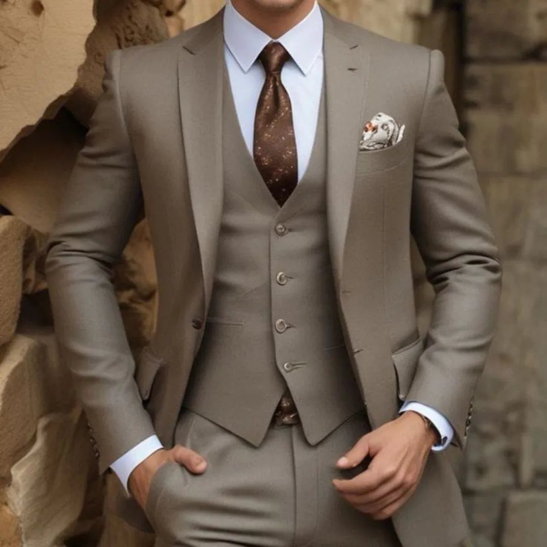 Man wearing a light taupe three-piece suit with a matching waistcoat and patterned brown tie.