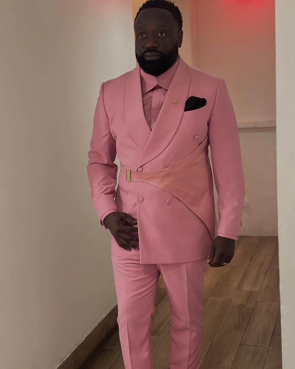 A man posing in a bright pink double-breasted suit with a matching belt and tie.