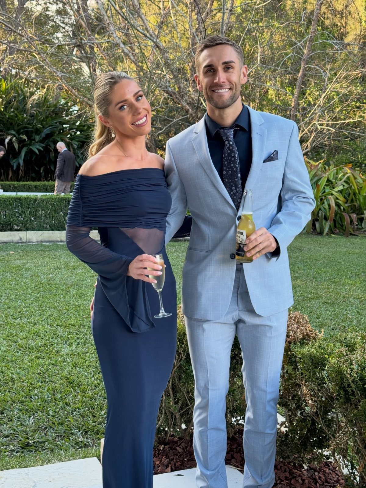 A man in a light blue suit and a woman in a navy dress smiling outdoors.