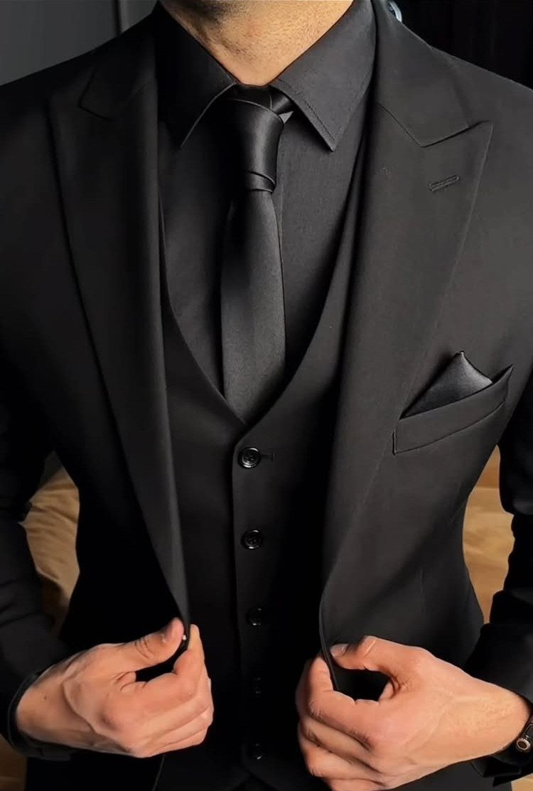 A man in a formal black three-piece suit with a matching tie and waistcoat.