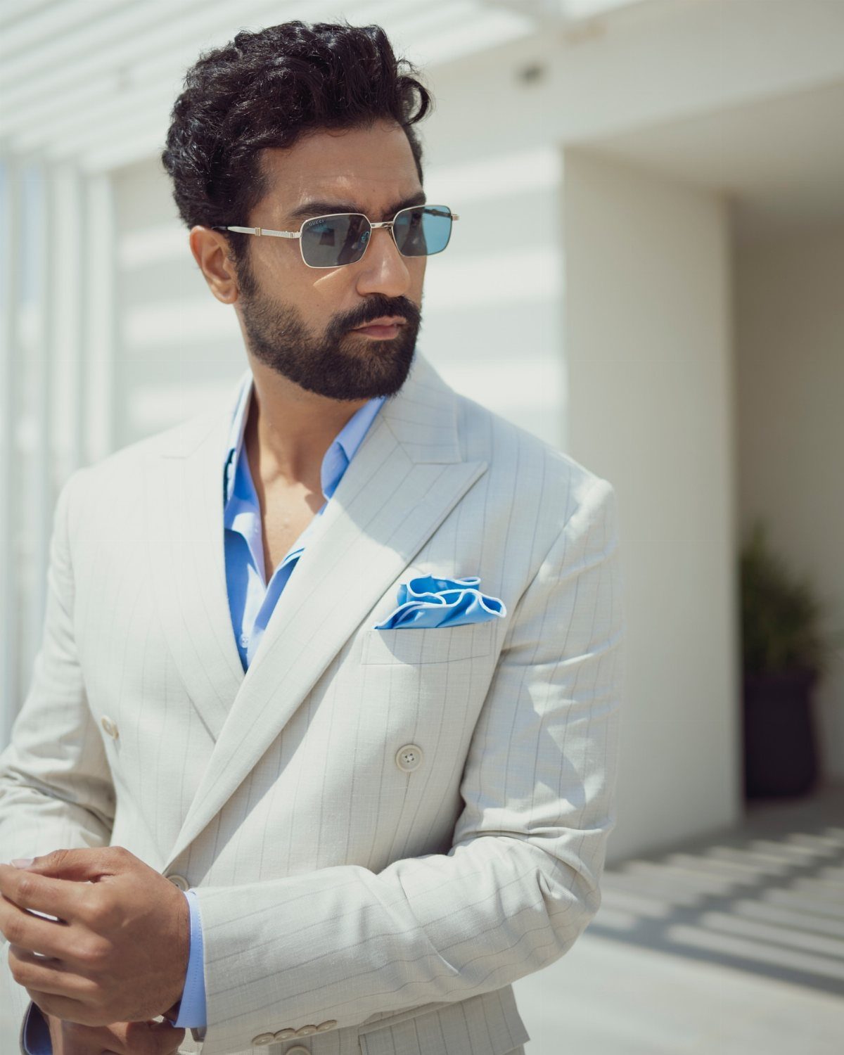 A man wearing a light beige pinstriped suit and blue shirt with sunglasses.